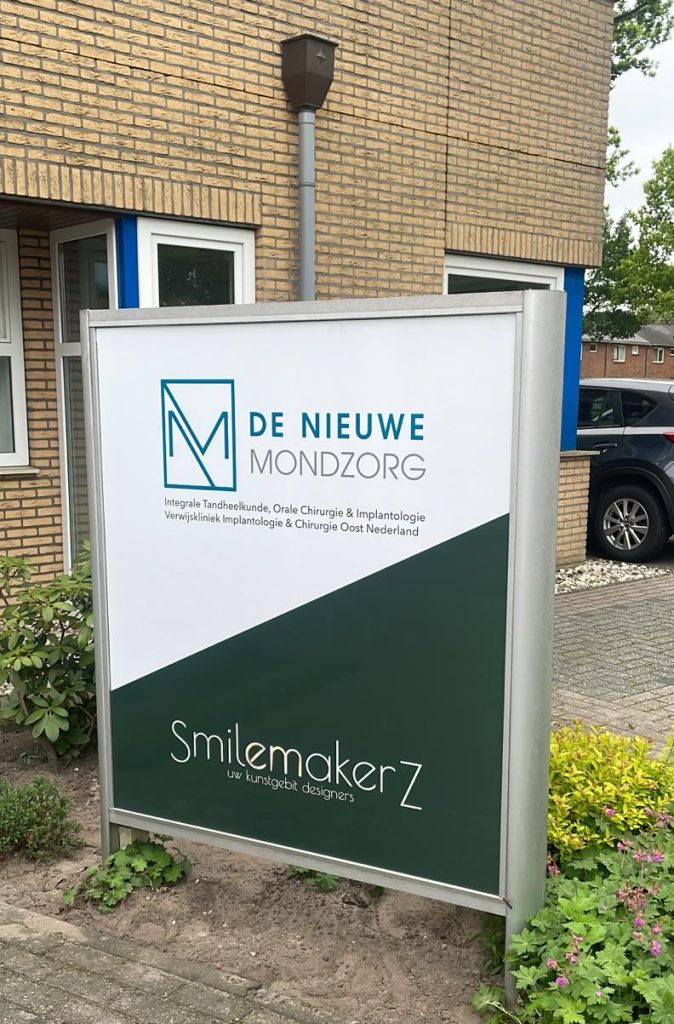 Sign featuring "De Nieuwe Mondzorg" and "SmilemakerZ" in a dental care context outside a clinic building.