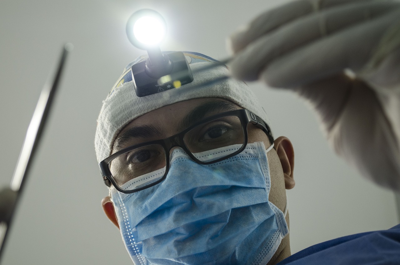 Een close-up van een chirurg met een hoofdlicht en een mondmasker, die gereedschap vasthoudt tijdens een operatie.